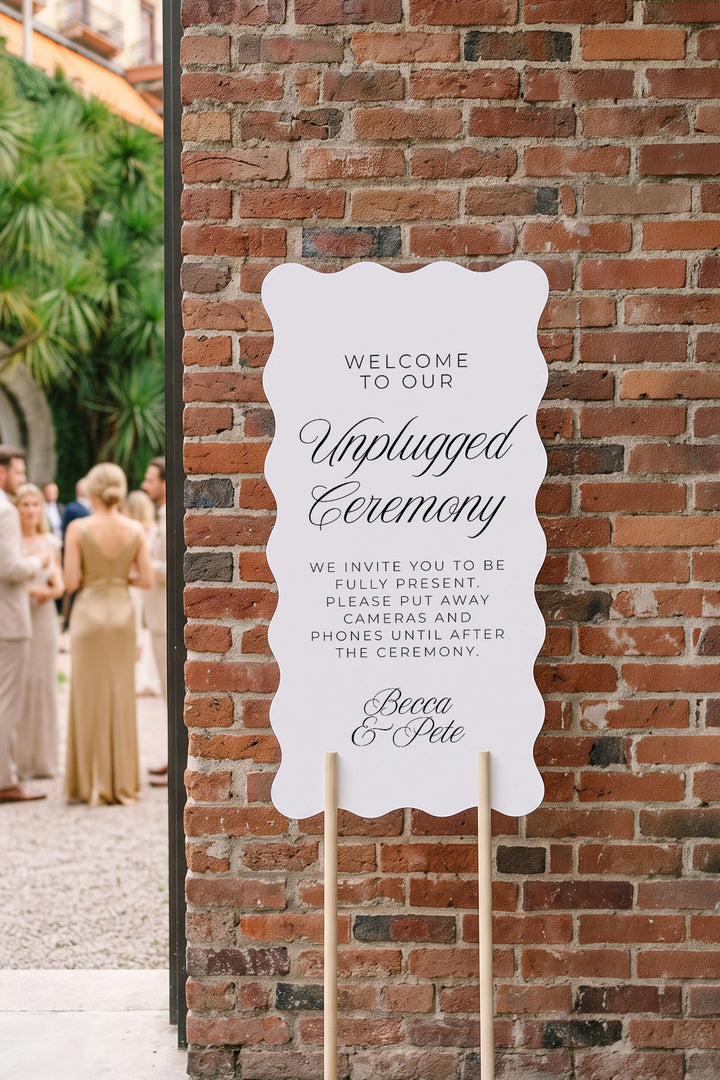Wavy unplugged ceremony sign on a wood stand against a brick wall at golden hour #shape_Wavy#size_Signature