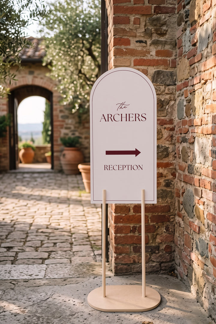 Linen off white arch reception directional sign in a courtyard beside a brick archway #color_Linen